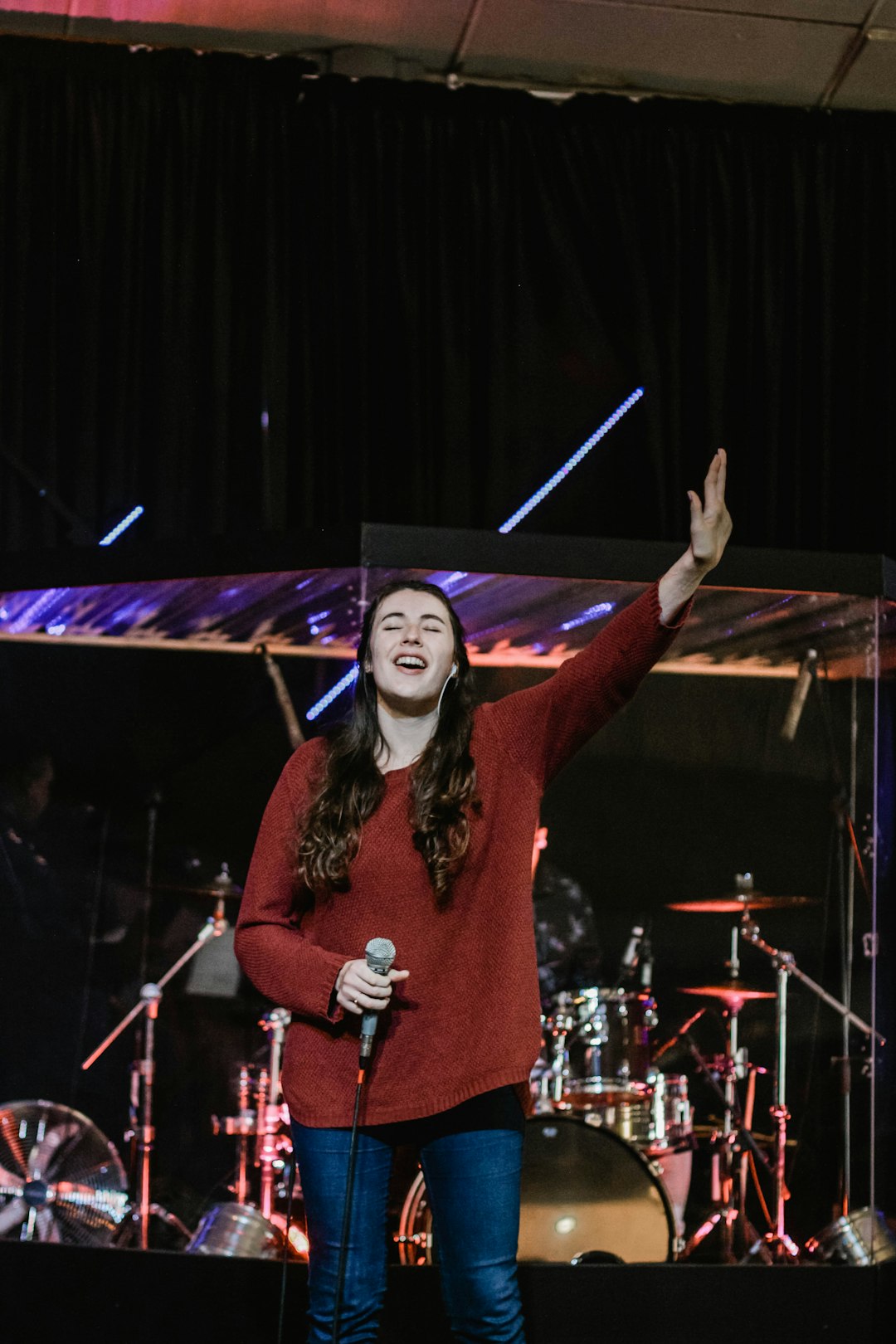 woman wearing red long-sleeved shirt holding gray microphone performing on stage