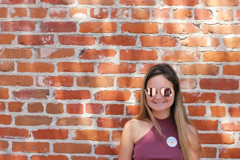 woman wearing sunglasses standing near brick building during daytime