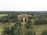 An aerial view of a large estate surrounded by dense greenery, featuring a grand building at the center. The area is filled with expansive lawns and a variety of trees, extending far into the horizon.