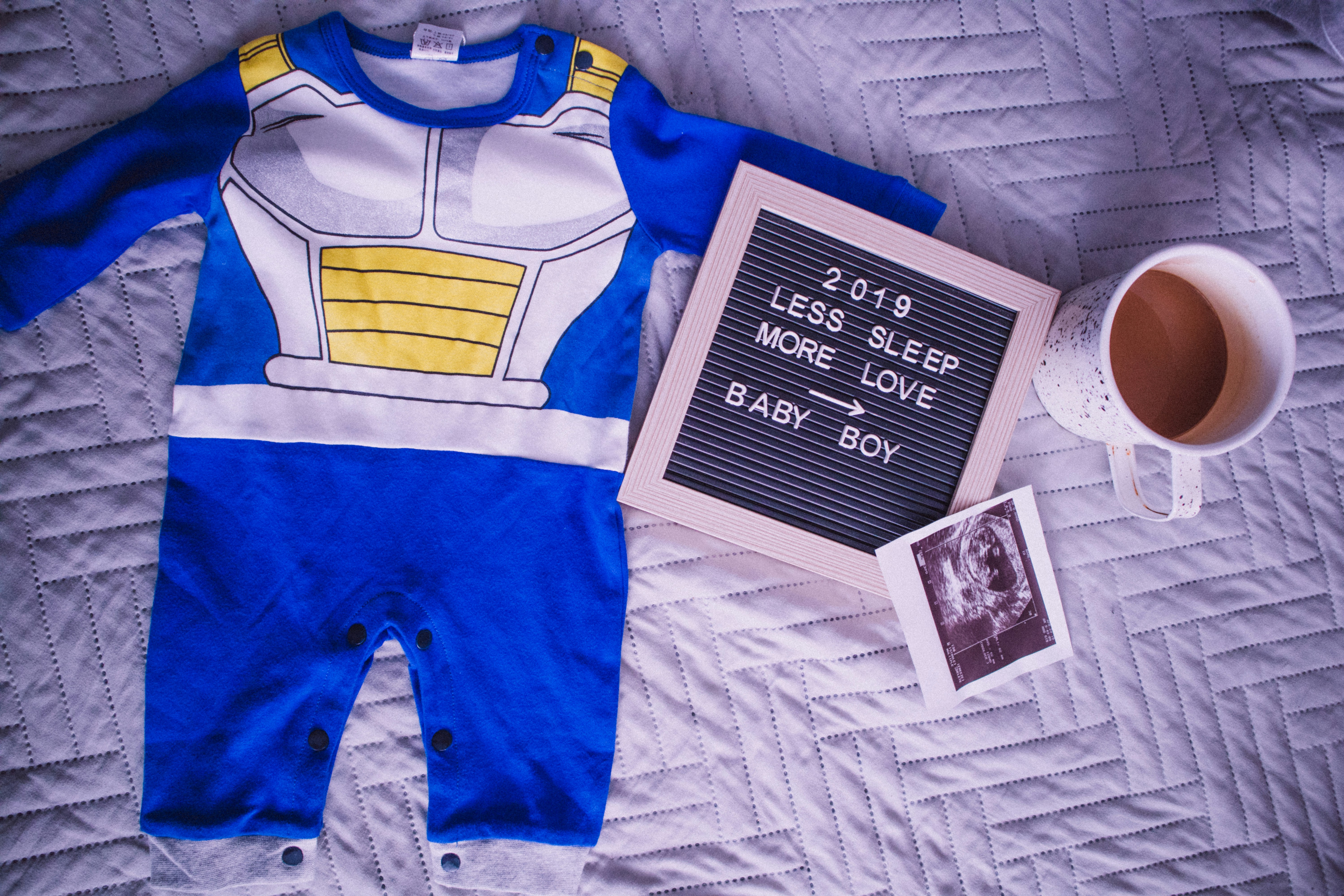 Urocza aranżacja dziecięcych ubrań chłopięcych, w tym niebieski śpioszek i maleńkie trampki.