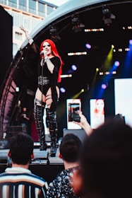 An artist smiling confidently while performing live on stage with dynamic red and black lighting.