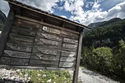 Trailhead signpost at the foot of a lush green mountain under a clear blue sky.
