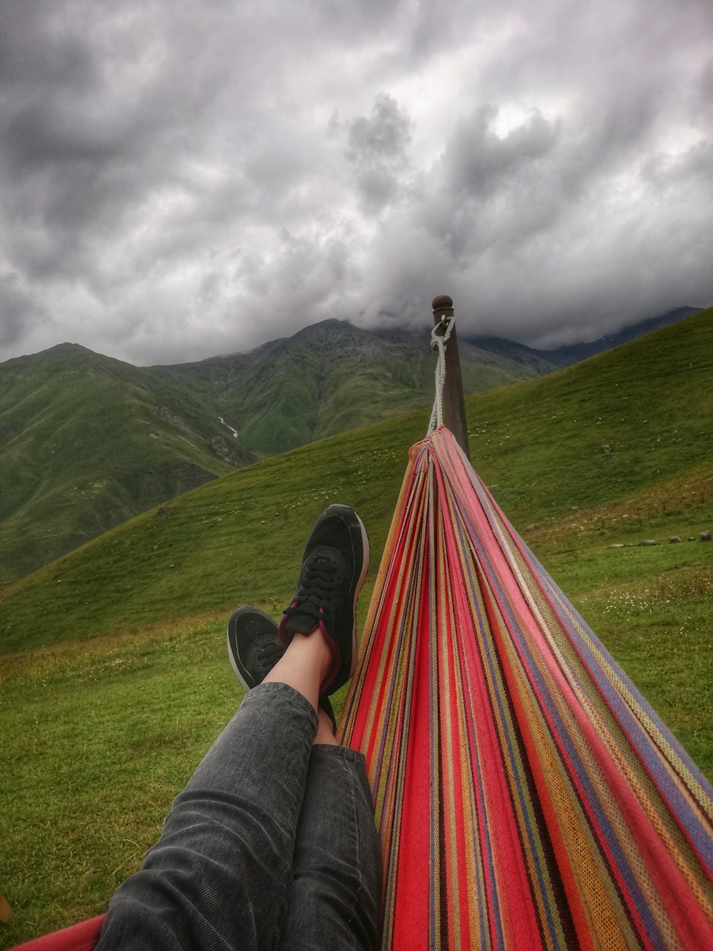 person wearing pair of black shoes on multicolored stripe hammock