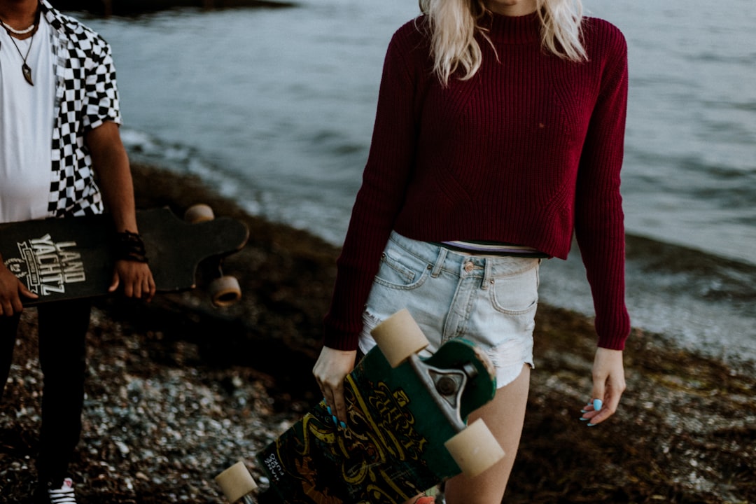 woman standing on seashore and holding longboard during daytime
