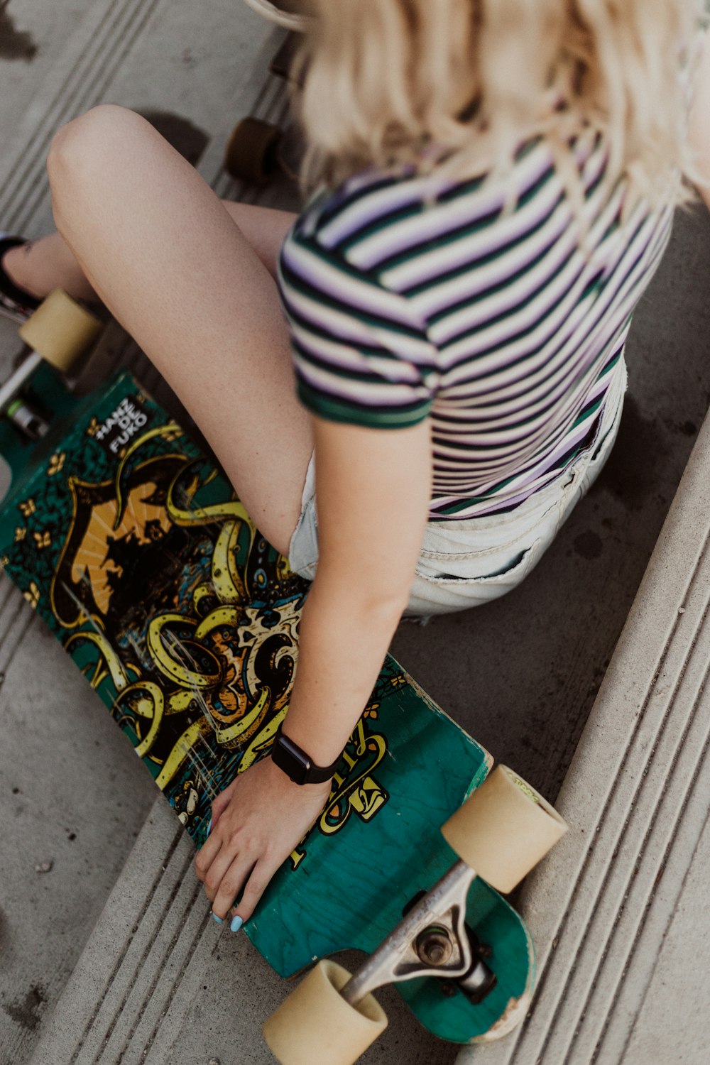 woman in striped shirt touching green skateboard