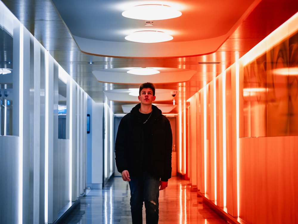 man wearing black jacket walking on red and silver hallway