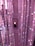 A close-up view of an LED strip light, attached to a transparent support, set against a background of numerous similar columns wrapped with glowing lights. The LED displays a soft pink hue, contributing to the overall ethereal ambiance.