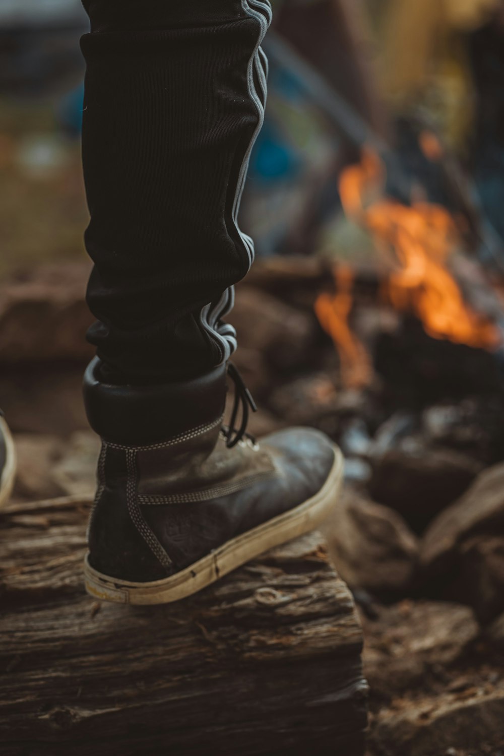 person in black pants and leather boots standing on wood near burning wood