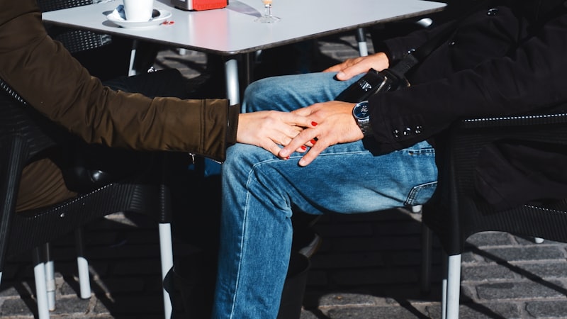Two people seated at a café table holding hands across their knees