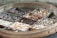 An assortment of spices is organized in a circular wooden tray. The spices are divided into separate sections using decorative, colorful fabric dividers, showcasing a variety of textures and colors.