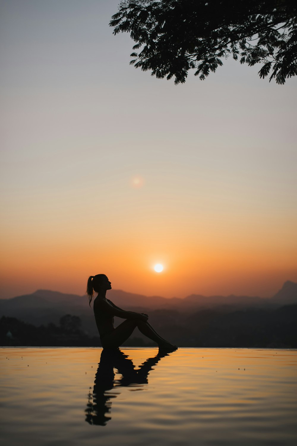 silhouette of woman sitting on edge of eternity pool during golden hour