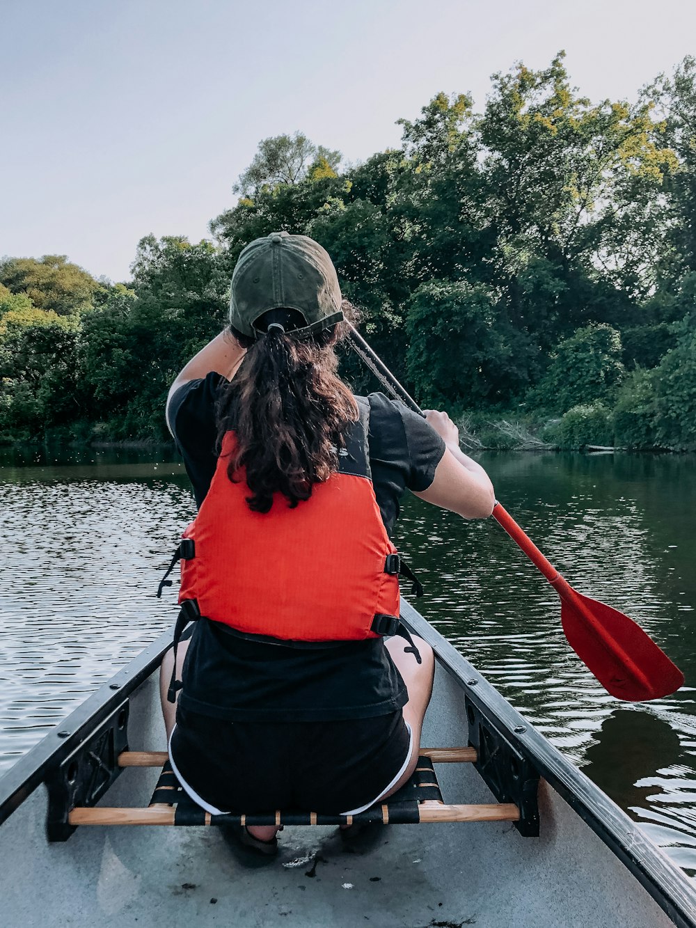 Una donna in un giubbotto di salvataggio rosso che pagaia una canoa