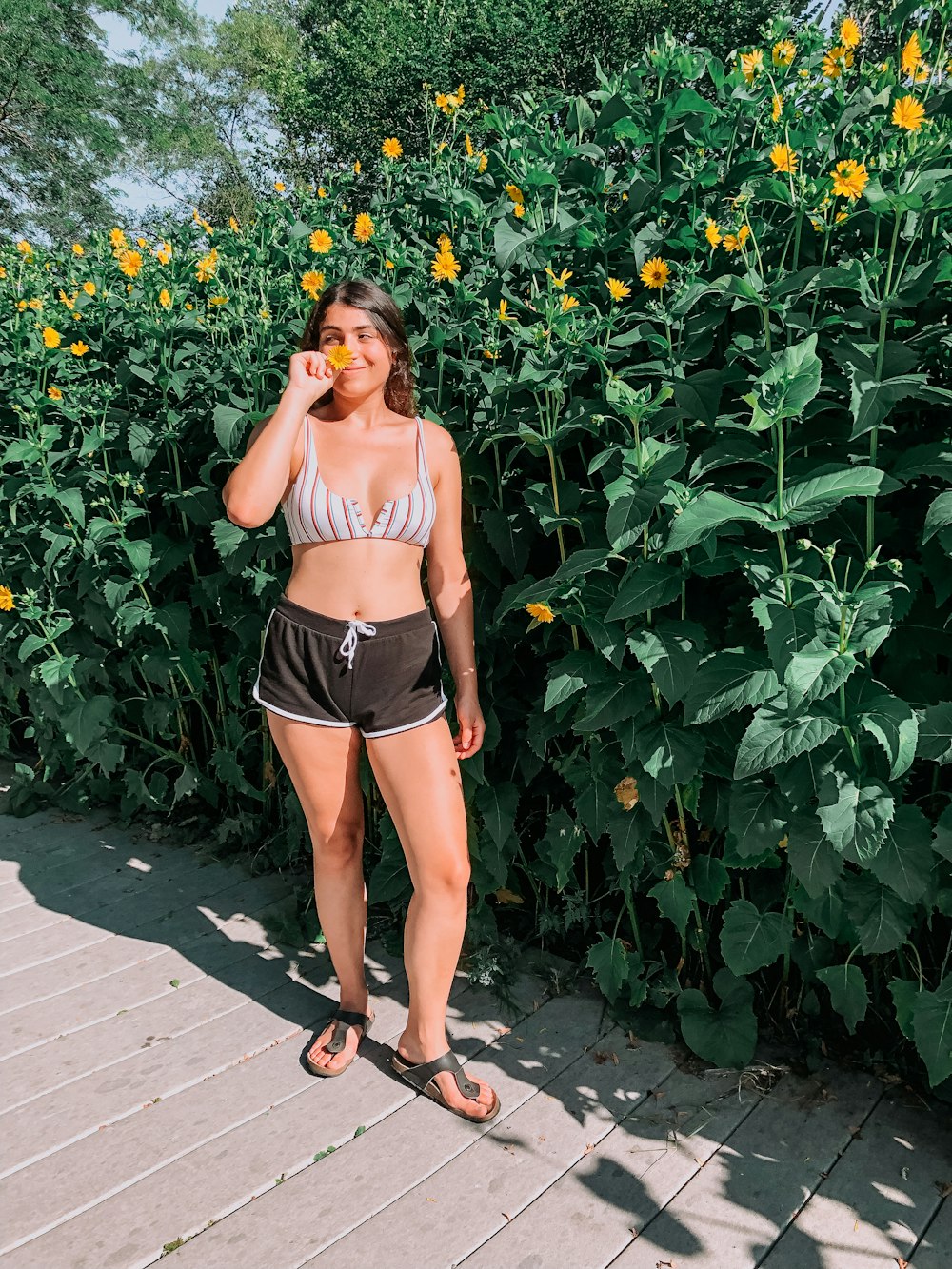 a woman in a bikini standing next to a bush of sunflowers