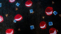 A dark patterned surface adorned with abstract designs, including red circular shapes resembling tennis balls, blue geometric cubes, and orange triangles. The design is scattered and repetitive, creating a visually engaging and playful motif.
