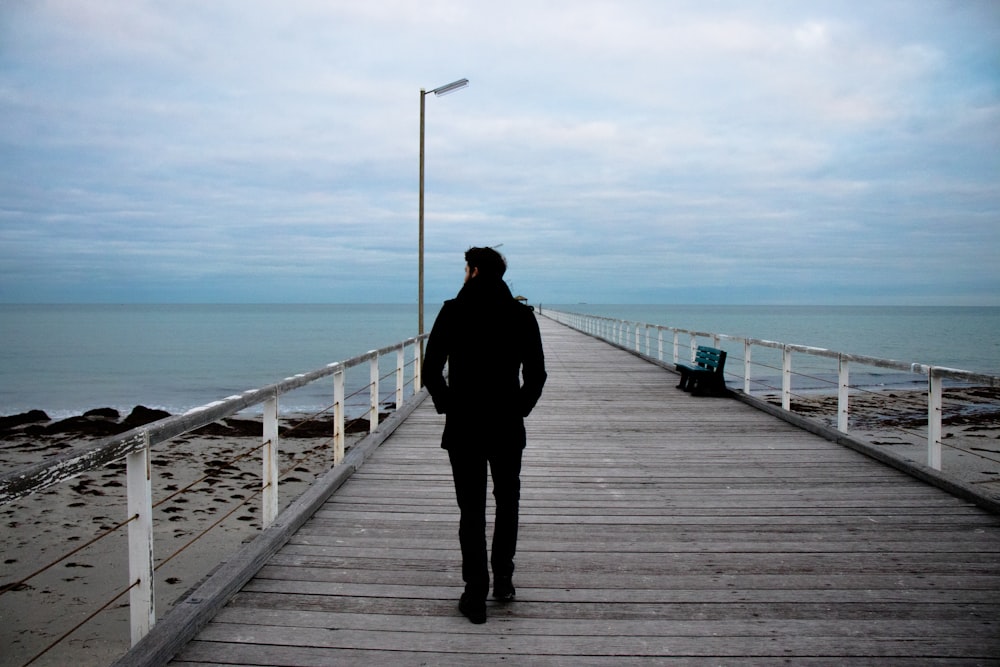 man standing on wooden dock beside seashore during daytime