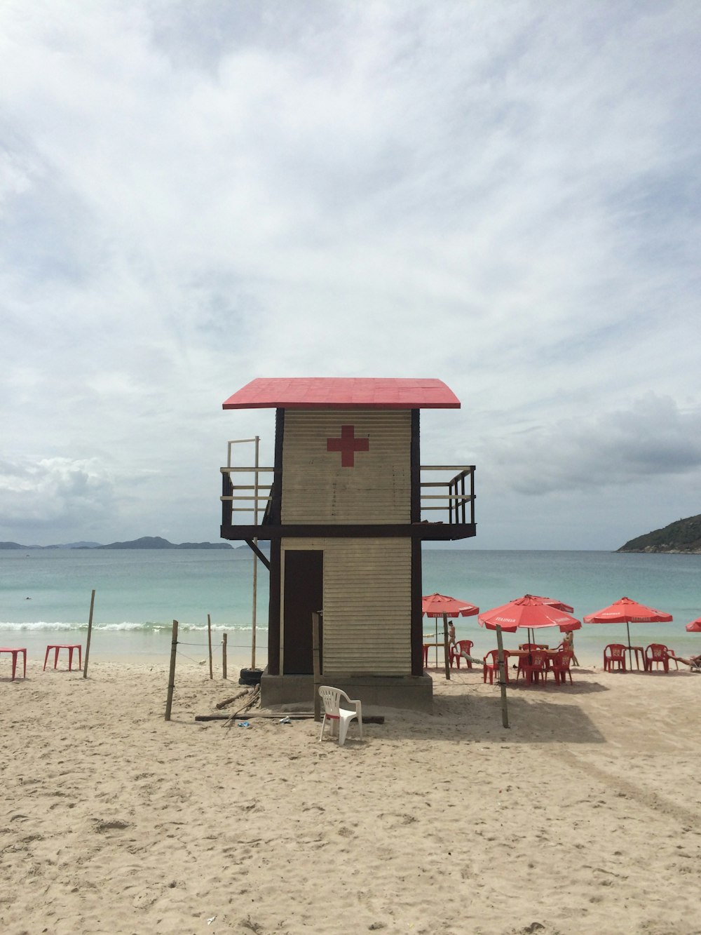 Casa de salvavidas blanca y roja cerca de sillas de playa rojas bajo cielos blancos