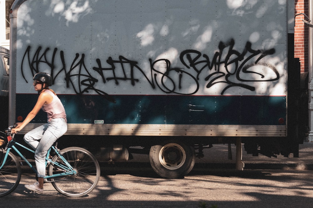 girl wearing pink tank top riding bicycle besides gray delivery truck