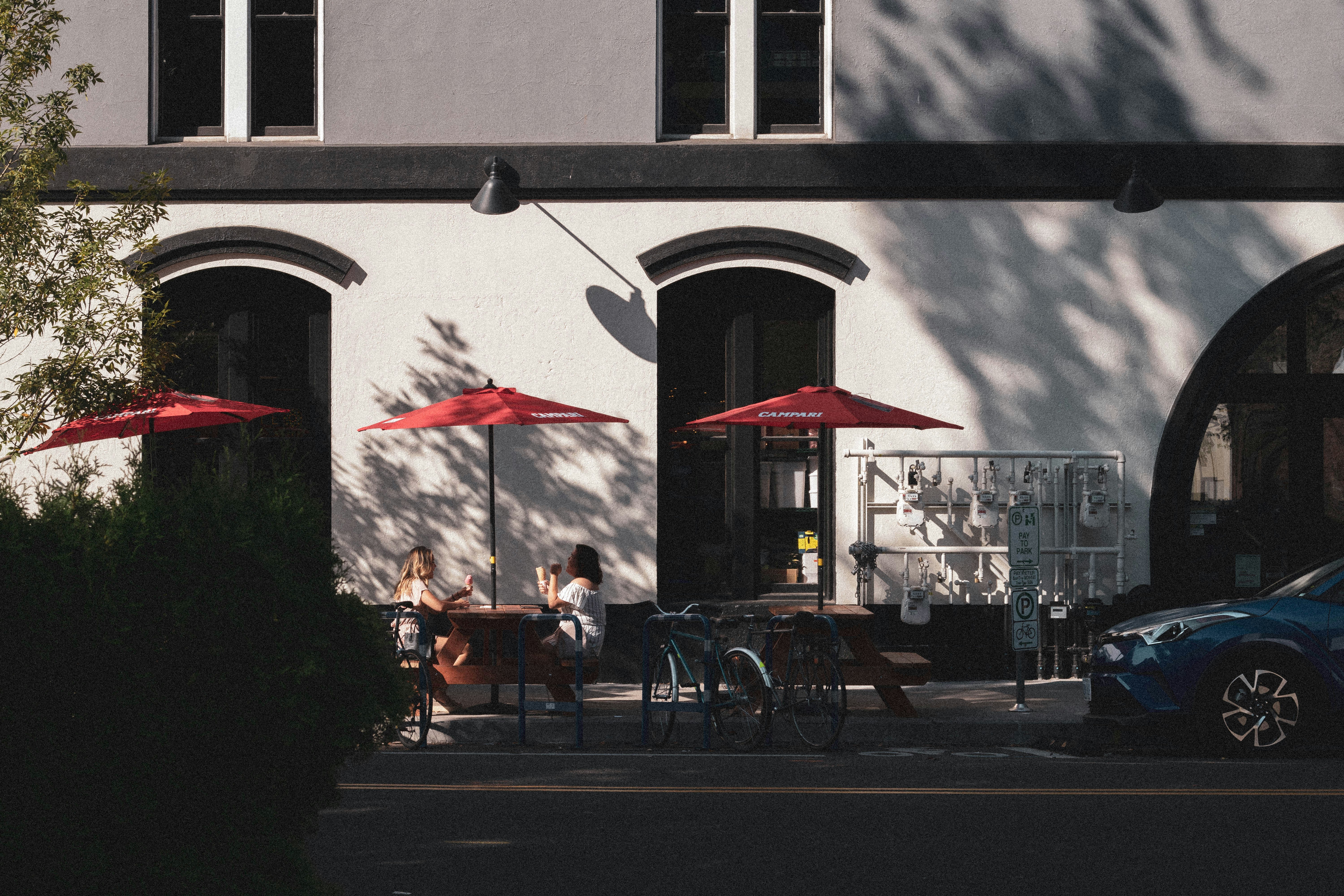 two person sitting under red patio umbrella beside the road