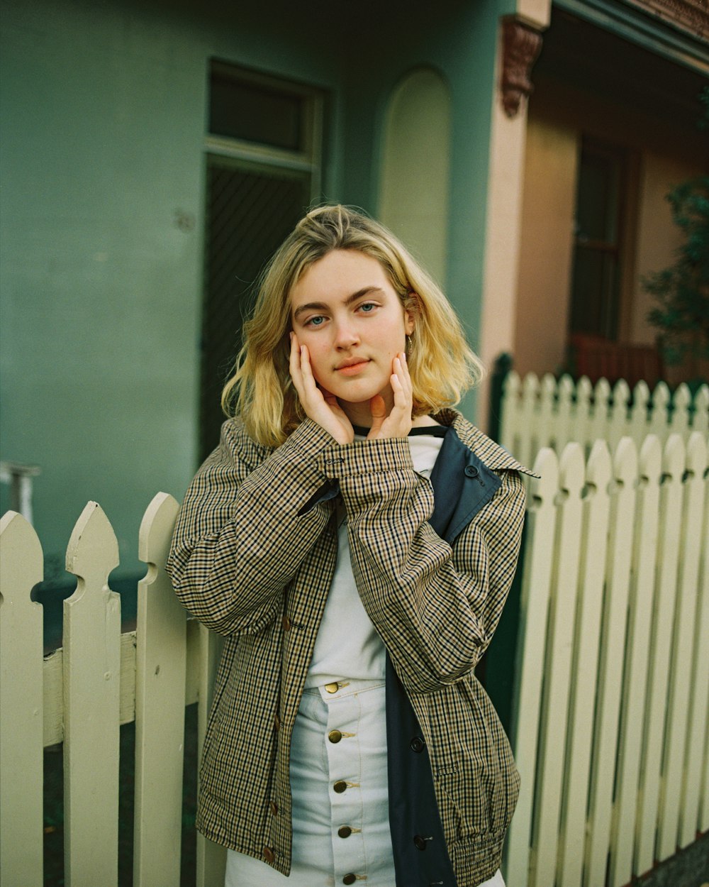 woman touching her face while leaning on wooden fence