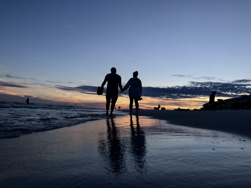 Silhouettenfotografie von zwei Menschen, die an der Küste spazieren gehen