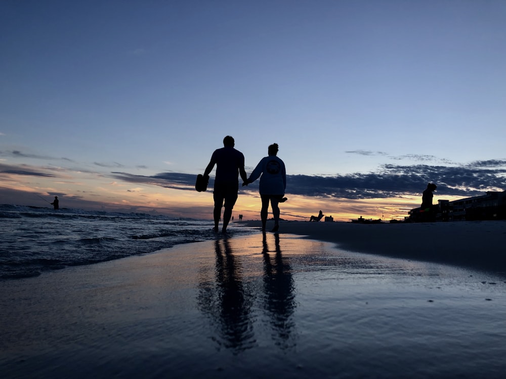 silhouette photography of two people walking on seashore
