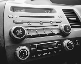A close-up view of a car's audio and climate control dashboard featuring buttons and knobs for tuning, volume, and air conditioning. The display shows 'AUX' and the time is 5:22.