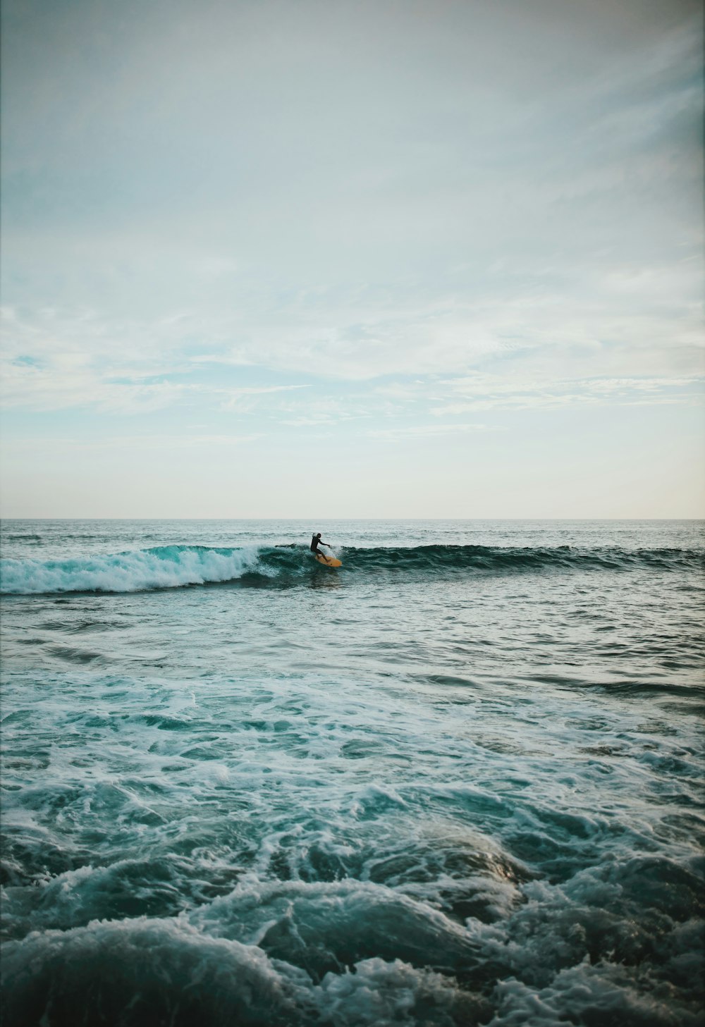 白い空の下、海でサーフィンをする人