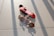 Two miniature skateboards are placed on a speckled, light-colored floor. One skateboard has a bright red top with a bold white design, while the other features an intricate, colorful pattern. The image is well-lit, casting defined shadows of the skateboards and their components onto the floor.