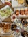 A variety of seafood dishes are artfully arranged on metal trays and plates over a wooden table. The spread includes fresh oysters on ice garnished with lemon wedges and dipping sauces, lobster rolls, crispy fried seafood, shrimp cocktail, and a Caesar salad with anchovies. Sea urchins with their distinctive spiky shells are also present, opened to reveal their contents. French fries appear in a tray accompanied by sauces. The setting suggests a casual and abundant seafood meal.