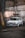 A vintage, white Volkswagen GTI is parked in an industrial setting against the backdrop of a weathered concrete wall with visible stains and cracks. The car features distinctive round headlights and custom white rims that give it a classic look. The ambiance is accented by dim industrial lighting and a rugged surface.