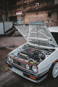 Dashboard view of a Volkswagen Golf 5 with the hood open in a suburban driveway.