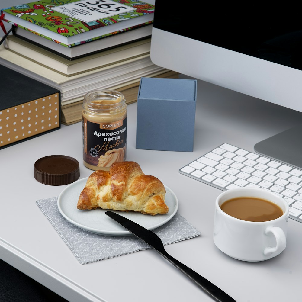 a white plate topped with a pastry next to a cup of coffee