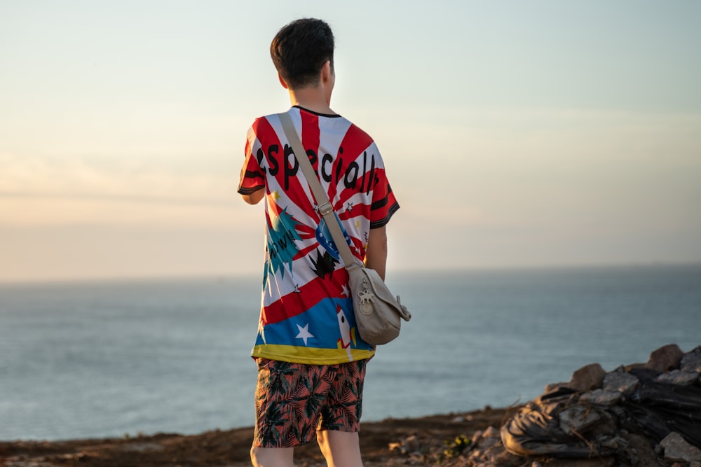 man with backpack standing beside body of water during daytime