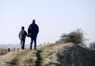 man and boy walking on grass near fence