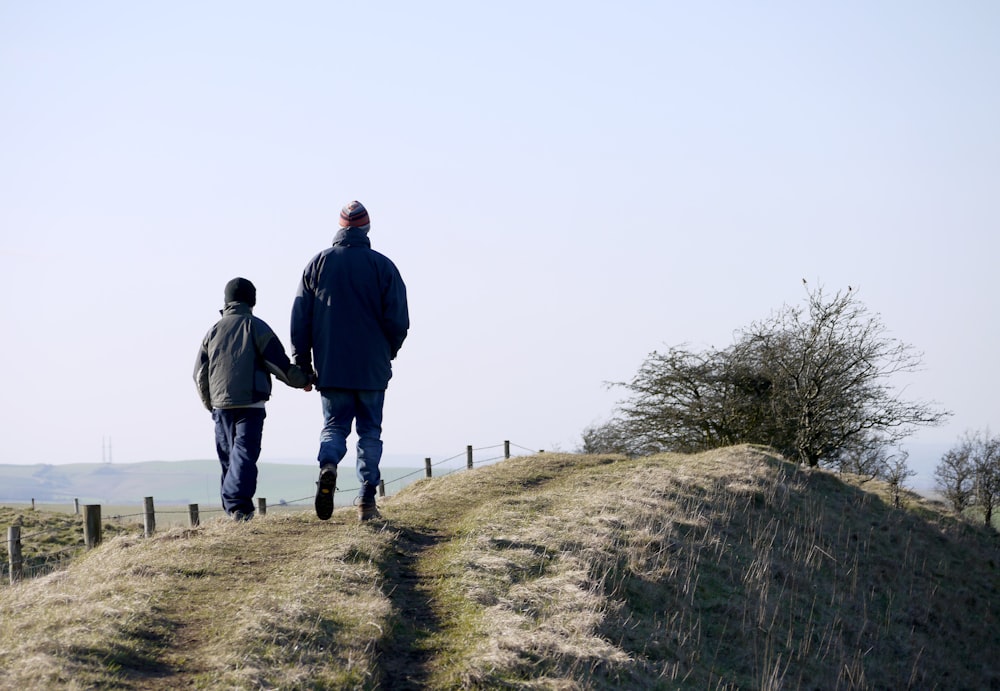 man and boy walking on grass near fence