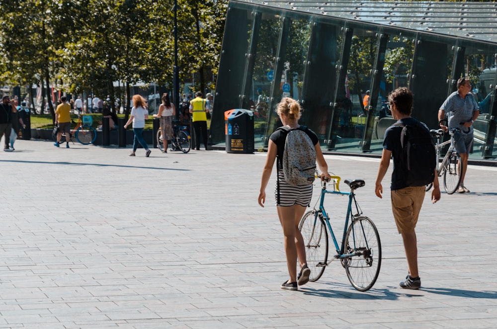 woman walking holding bicycle near man