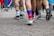 A group of people walking on a cobblestone street, wearing colorful socks and sneakers. The focus is on their legs and feet. Vibrant rainbow patterns on the socks suggest a theme of celebration and unity. The crowd seems to be part of a larger gathering or event.