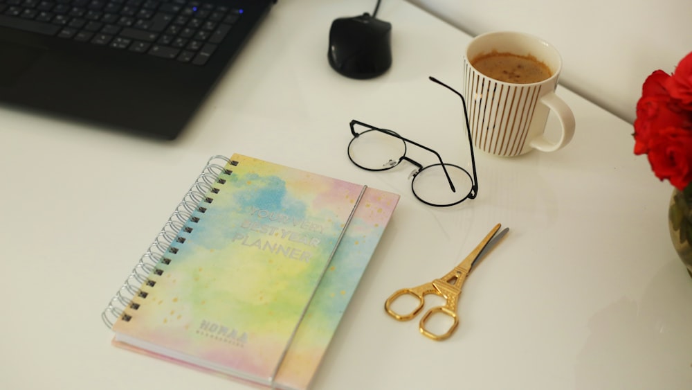 spring notebook beside eyeglasses scissors and cup of coffee