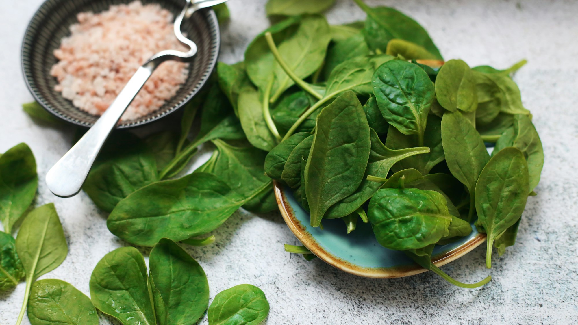 a plate of spinach and a bowl of pink salt