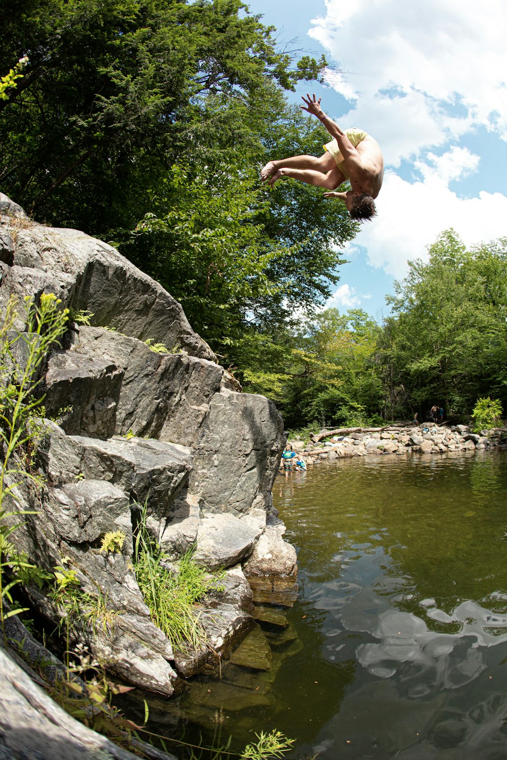 person jumping from boulder to body of water during daytime