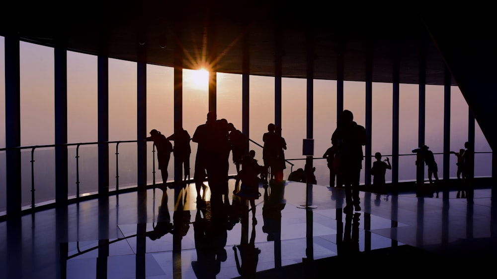 silhouette of standing people viewing through glass wall during golden hour