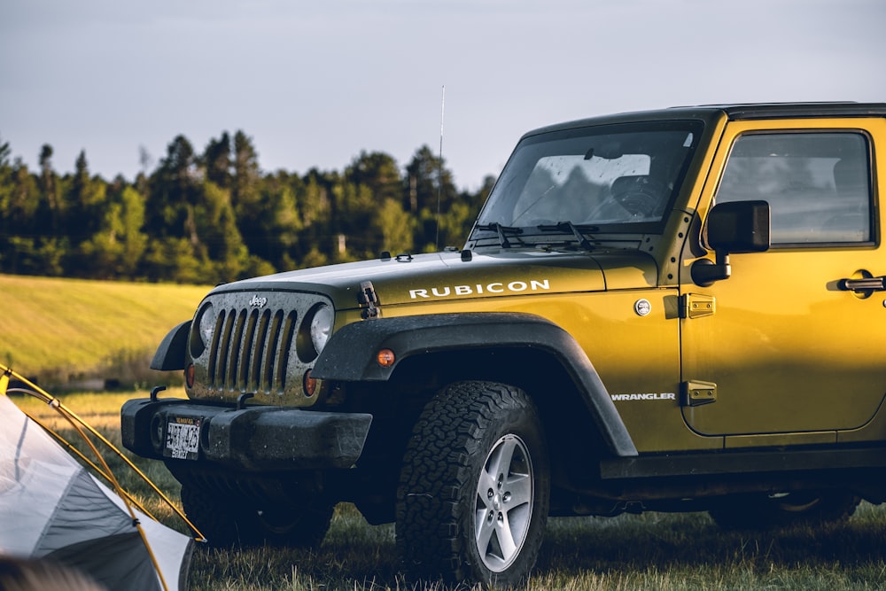 yellow Jeep Wrangler Rubicon on grass field near tent during daytime