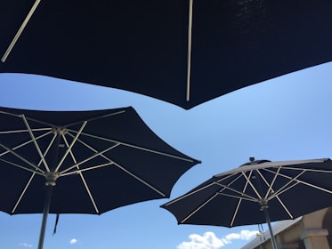 Several large black umbrellas with metallic spokes are opened under a clear blue sky. A few clouds are visible in the background, and a structure is partially seen in the lower right corner.