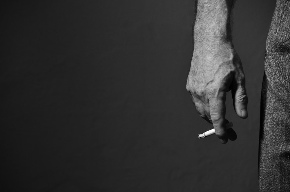 grayscale photo of person's right hand with lighted cigarette