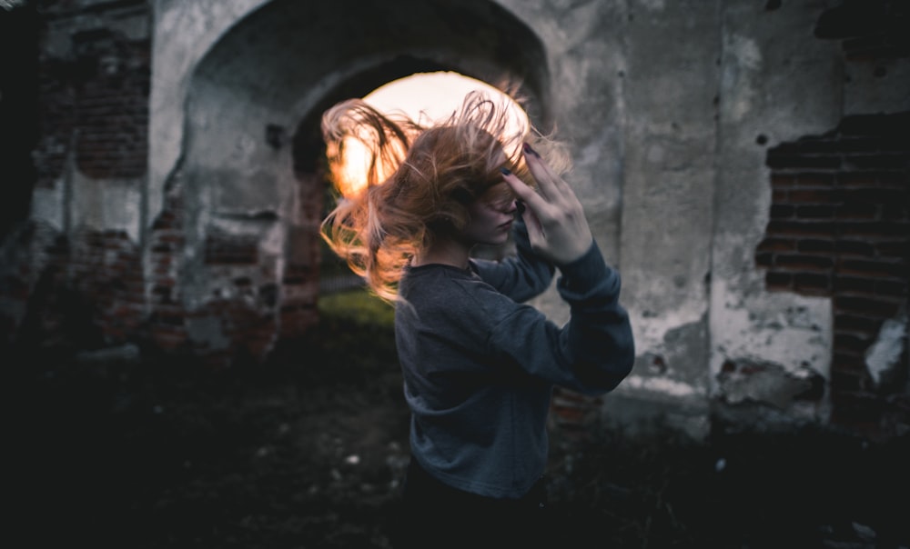 femme en chemise grise à manches longues retournant les cheveux