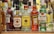 A collection of various liquor bottles is displayed on a shelf. The bottles include brands like Campari, Jim Beam, Finsbury, Aperol, and Bacardi. Each bottle is distinct in shape and color, with labels showcasing their logos and brand names.