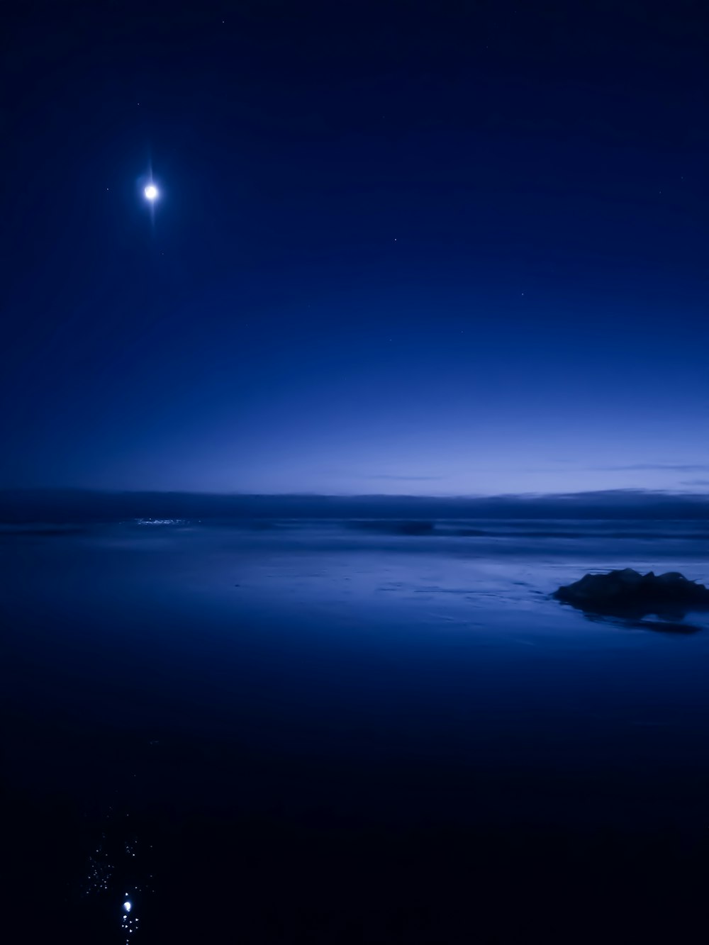 a full moon is seen above the ocean at night