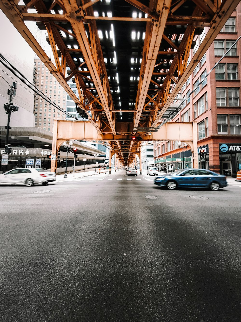 blue sedan under brown metal bridge