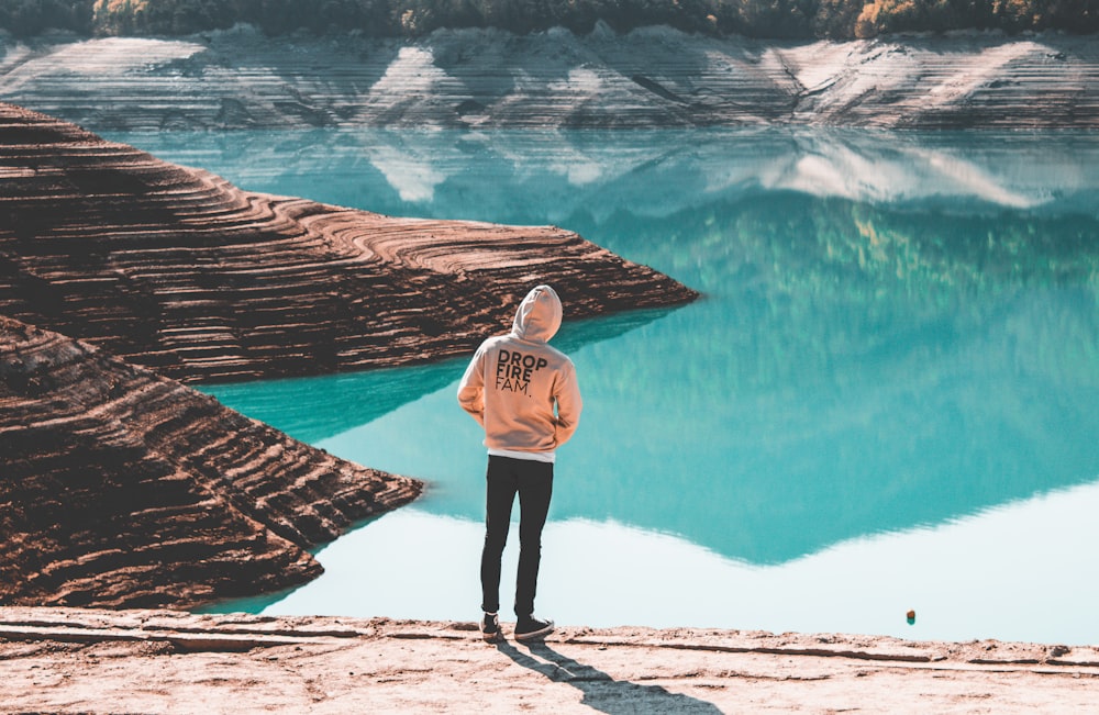 person wearing brown hooded jacket standing near blue ocean