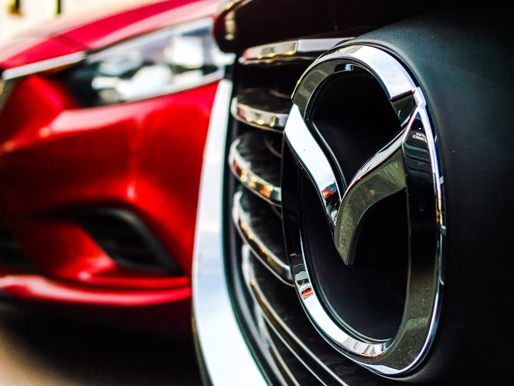 Emblema de Mazda en la parrilla junto a un coche rojo aparcado